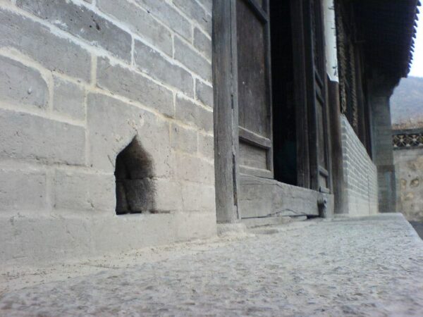 A cat’s eye view of a small opening—perhaps a cat door?—in the gray brick outer wall of a traditional Qing Dynasty wood-and-brick courtyard house in Cuandixia Village, Mengtou District, Beijing.