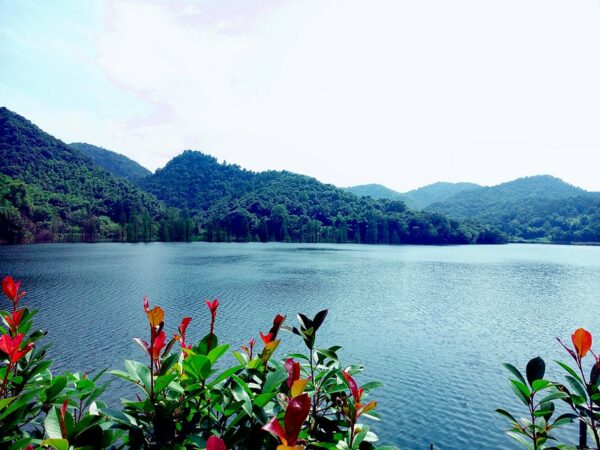 Red and green foliage in the foreground and heavily forested deep green hills in the background frame the dark blue waters of Shitan Reservoir.