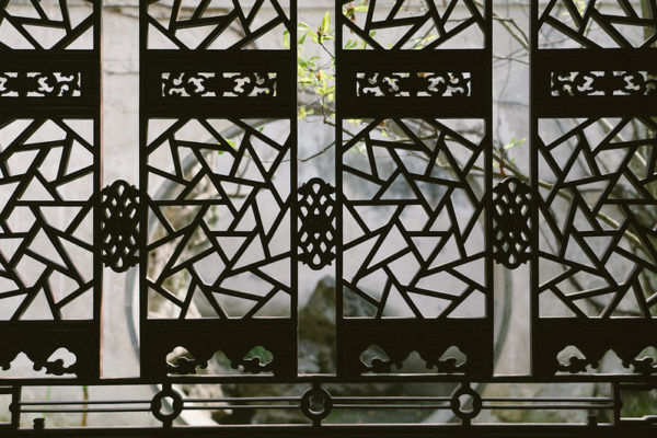 A moon gate and tree branches viewed through a carved wooden screen