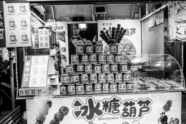 A woman with a small stall sells “bingtang hulu,” a traditional Chinese snack of candied Chinese hawthorn fruits on a bamboo skewer.