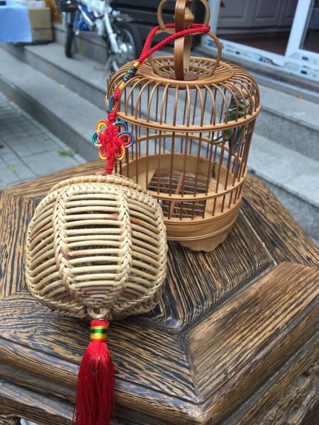 Two wooden cricket cages decorated with traditional red silk knots adorn a small, hexagonal wooden table.