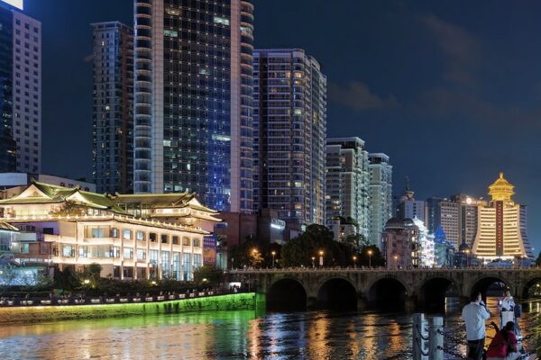 Guiyang’s nighttime cityscape is dominated by a lakeshore lined with tall buildings—some modern glass skyscrapers and some with traditional Chinese architectural features—whose lights are reflected in the surface of the lake.