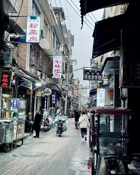 In the Muslim quarter of Xi’an, China, a busy, narrow alley is bustling with motorcycles, passersby, shoppers, food stalls, colorful signs and two-story buildings strung with visible power lines.