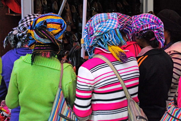 A group of women with colorful sweaters, purses, and headscarves cluster around a display of shoes at a market in Lhasa.