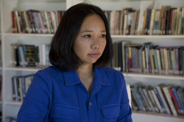 The author, wearing a vivid blue collared shirt, seated in front of a row of bookcases. 