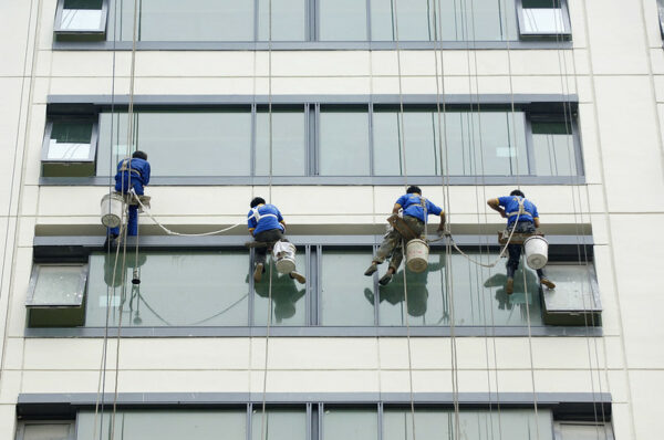 Four blue-shirted workers, wearing harnesses attached to long ropes, wash the windows of a multi-story building in Beijing.