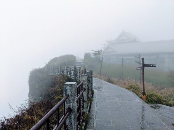 Mist cloaks a stone-paved path leading up to a temple at the edge of a cliff.