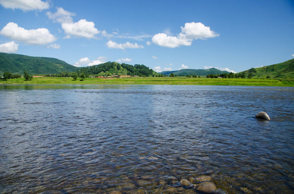 Stones are visible beneath the rippling surface of the Yalu River. On the opposite bank is a series of low, verdant hills.